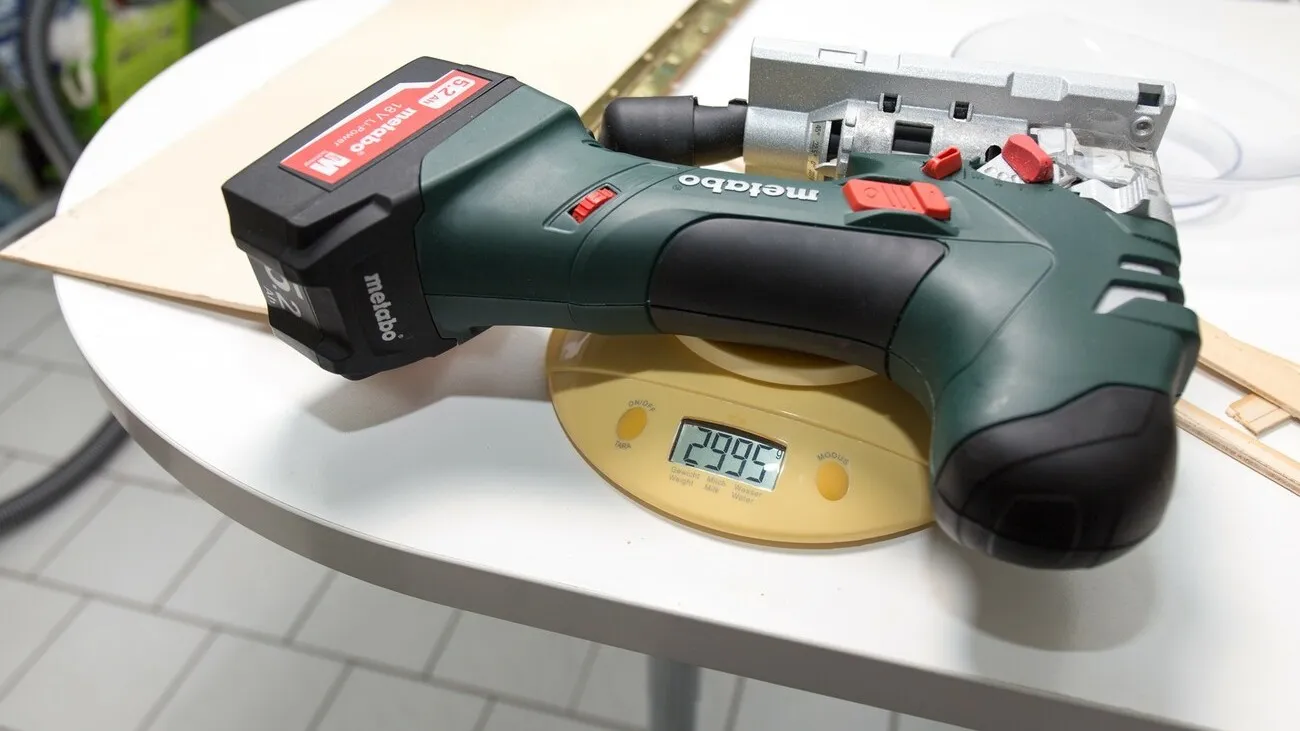 Die Metabo Stichsäge liegt auf einem weißen Tisch auf einer gelben Waage. Die Waage zeigt 2995g an.